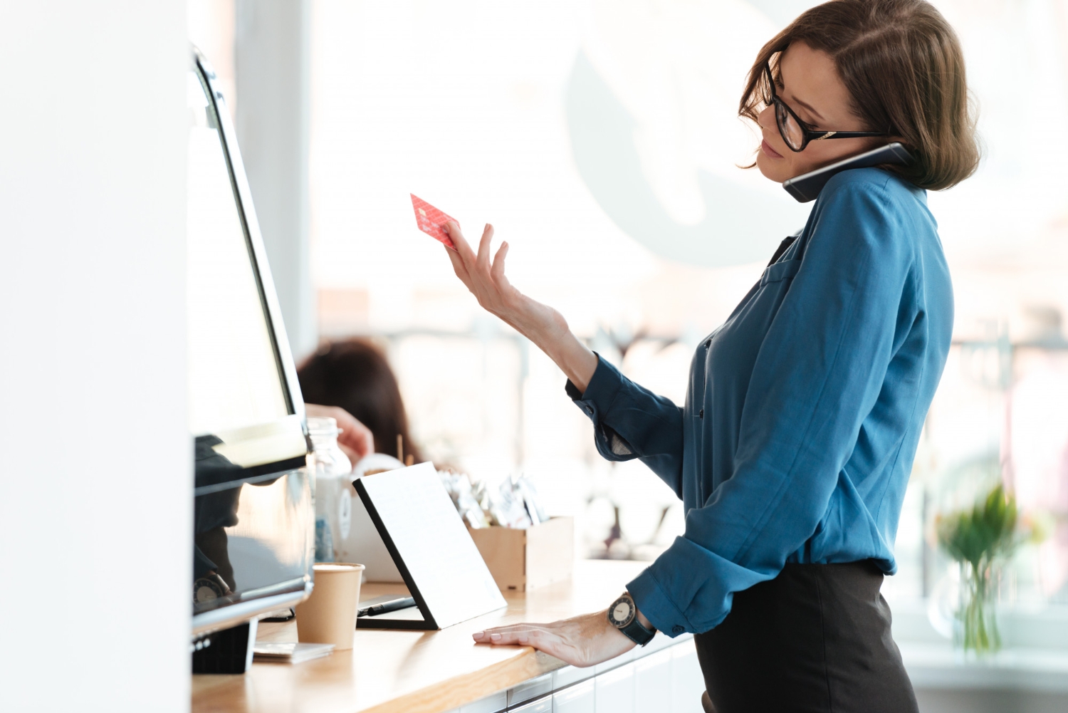 woman-standing-in-cafe-holding-credit-card-talking-by-phone (1) - Velfix